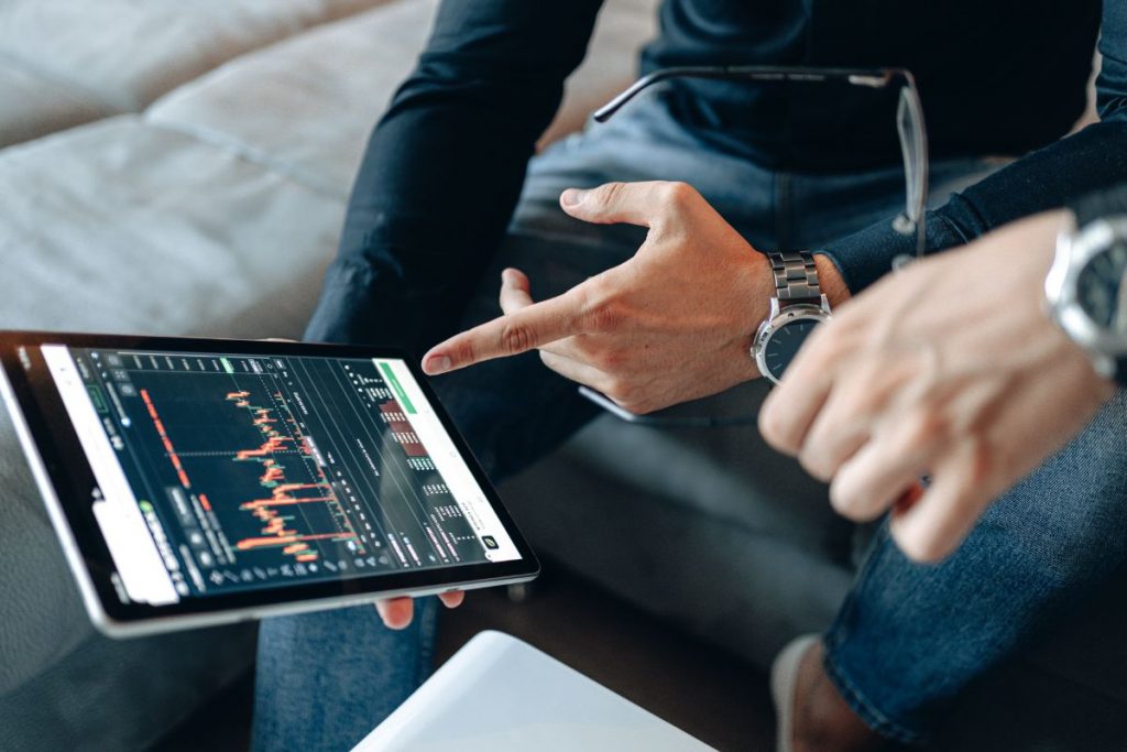 Two people sitting on a couch looking at a tablet with a stock chart on it.
