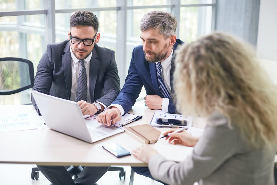 Three business people sitting around a table looking at a laptop.