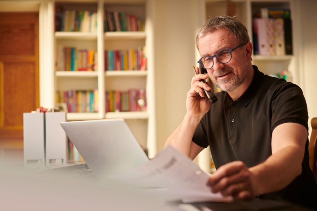 A man is talking on the phone while sitting at a desk.