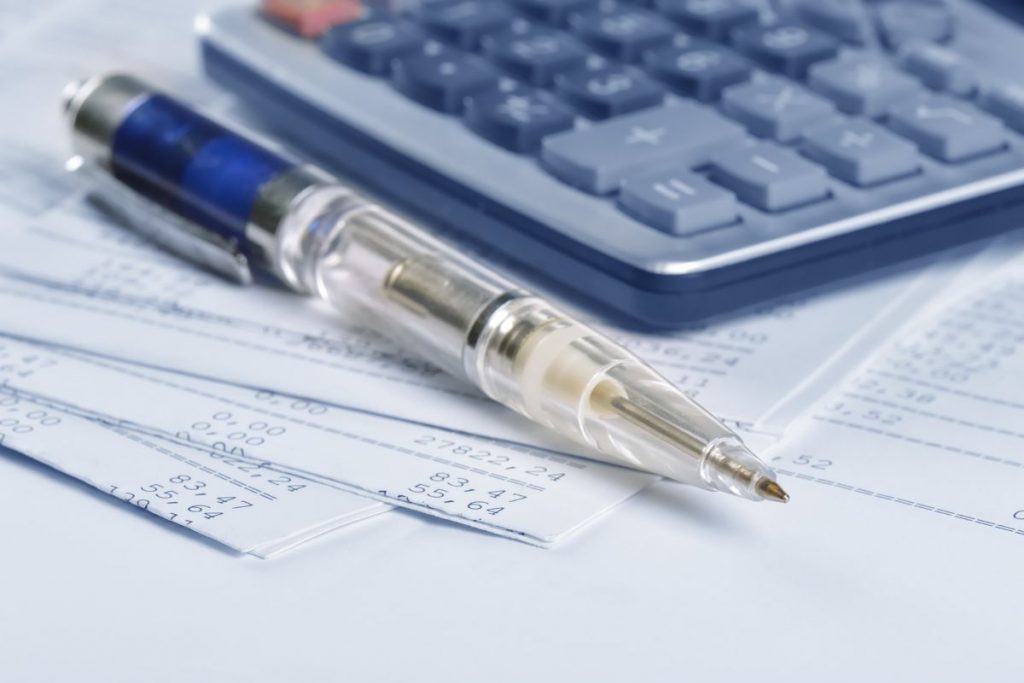 A pen sits on top of a calculator and papers.