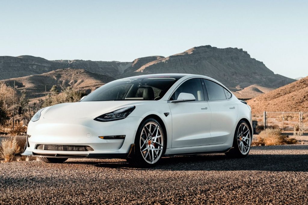 A white tesla model 3 parked in a desert.