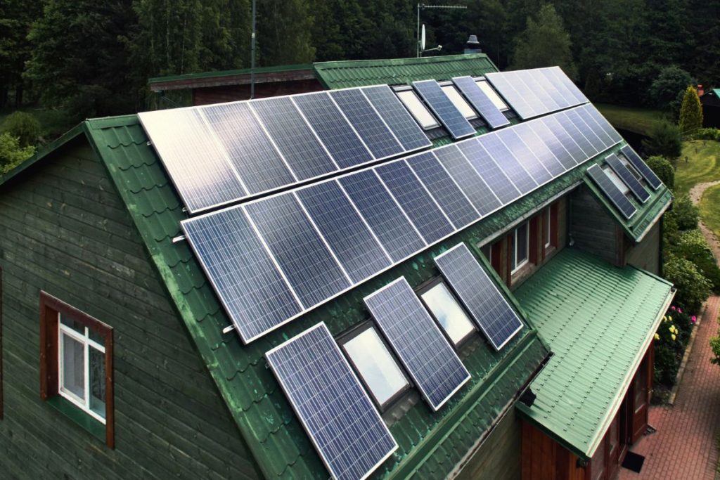 A row of solar panels gleams on the green roof of a wooden house, nestled among the trees, a reminder of how My Personal Tax CPA emphasizes environmental sustainability with the added benefit of solar panel tax credit