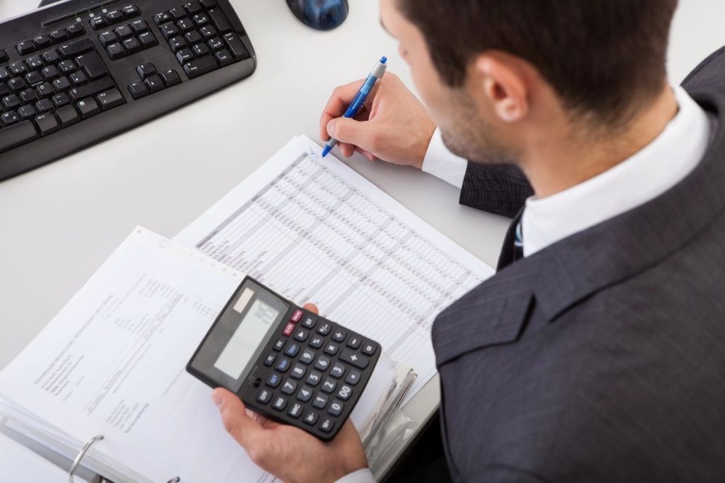 A person in a suit diligently calculates the Solo 401k tax credit for new enrollments, carefully entering figures onto a spreadsheet.