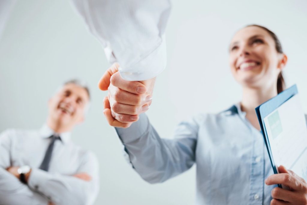 Two people in business attire shake hands, while a third person smiles in the background. The handshake symbolizes a successful agreement, possibly about Employee Stock Options, reflecting collaboration and mutual benefit