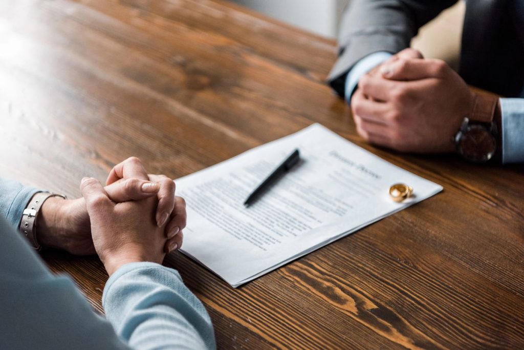 Two people sit across a wooden table with a divorce decree, wedding rings, and a pen between them, suggesting a discussion of divorce and important matters like filing taxes after divorce..
