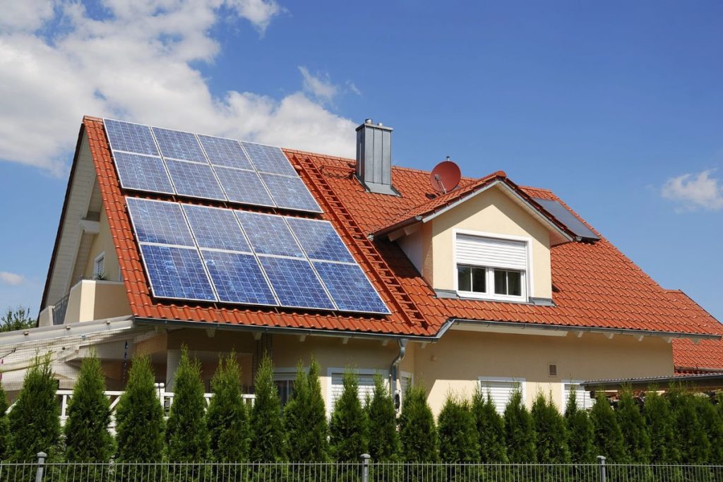 A house with a red-tiled roof has several solar panels installed on one side, taking advantage of the credits before the 2026 Home Energy Credit Sunset, all under a clear blue sky.