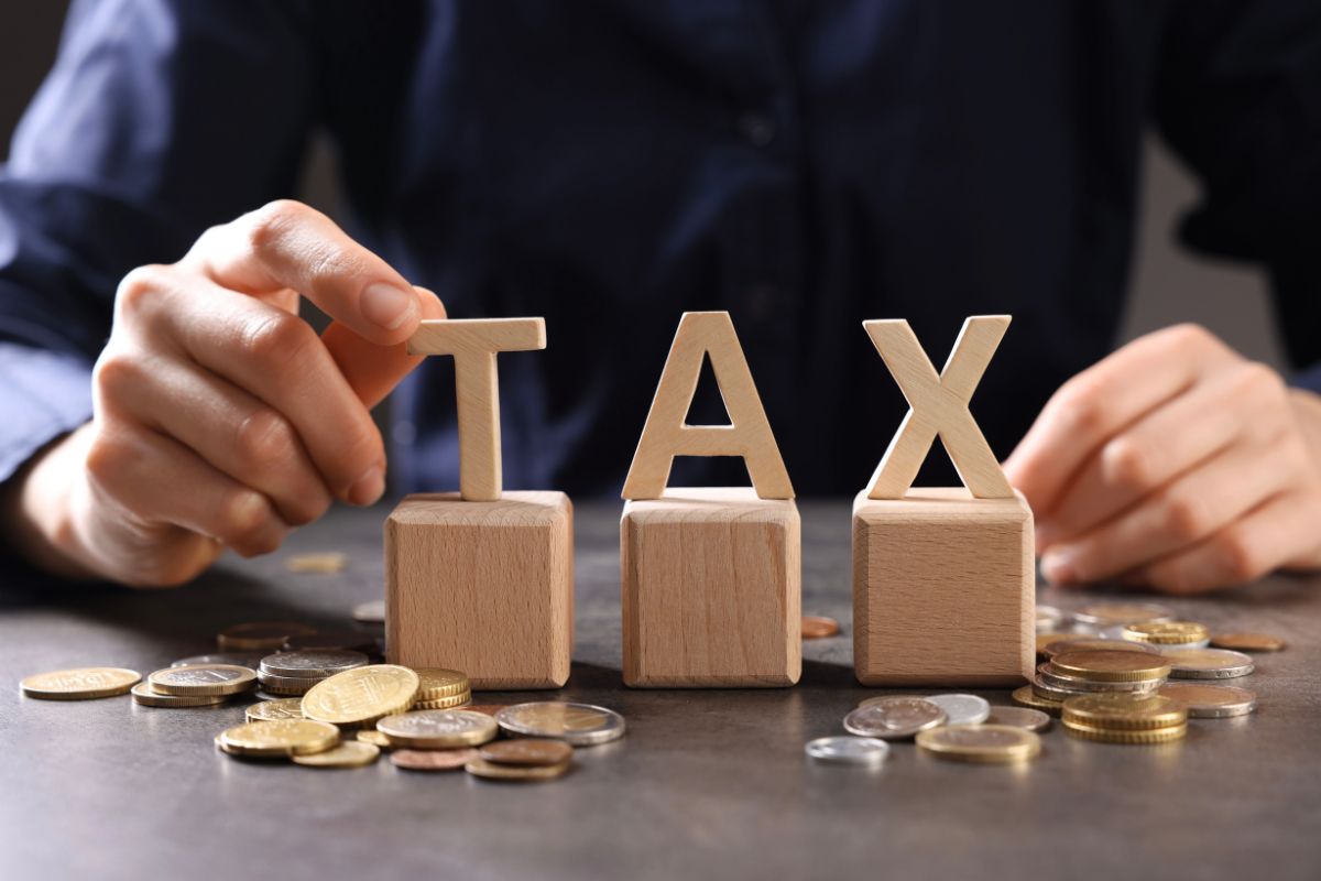 A person arranges wooden blocks spelling "TAX" surrounded by scattered coins on a table) representing that IRS paper checks ending in 2026.